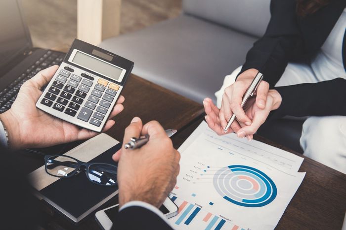 A man is holding a calculator and a woman is writing on a piece of paper.