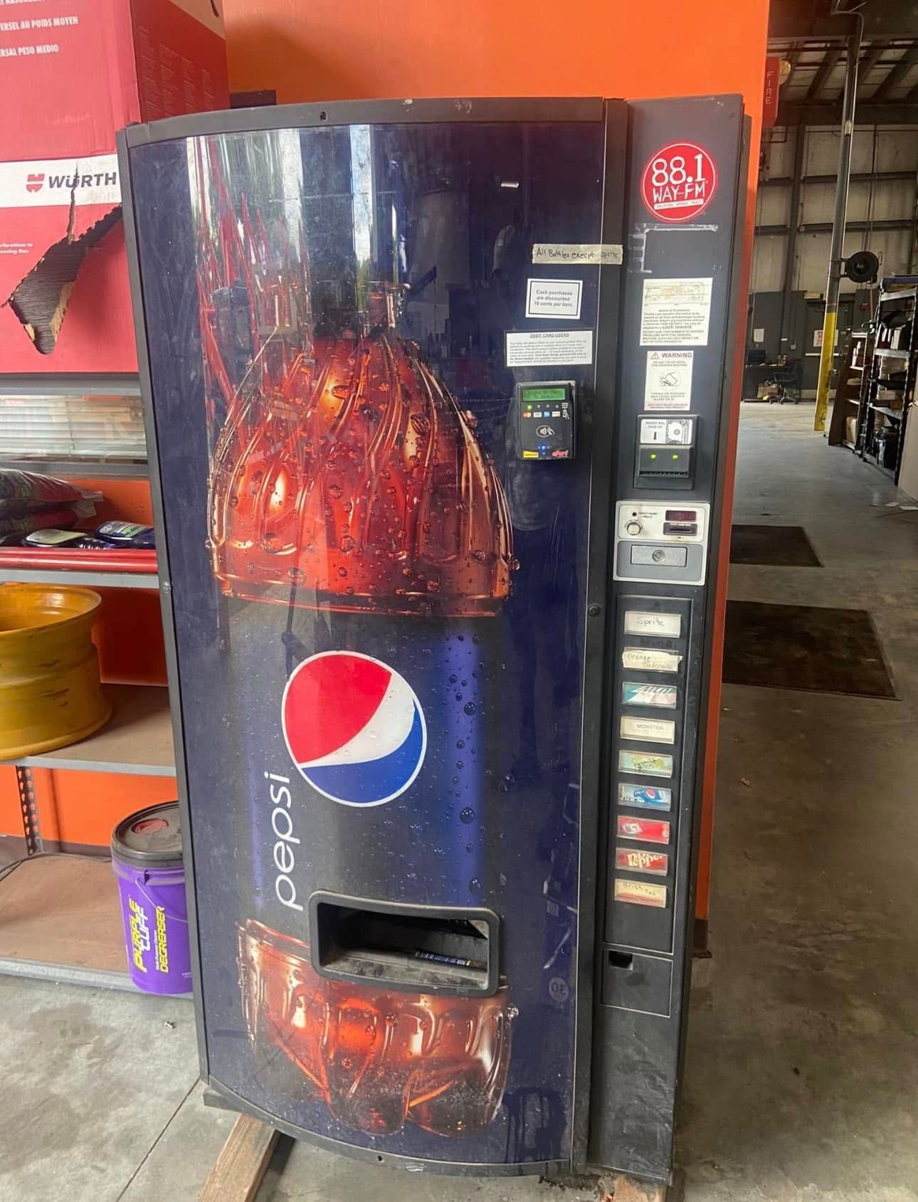 A dark blue Pepsi vending machine with an image of ice-filled glasses, standing in a warehouse setting.