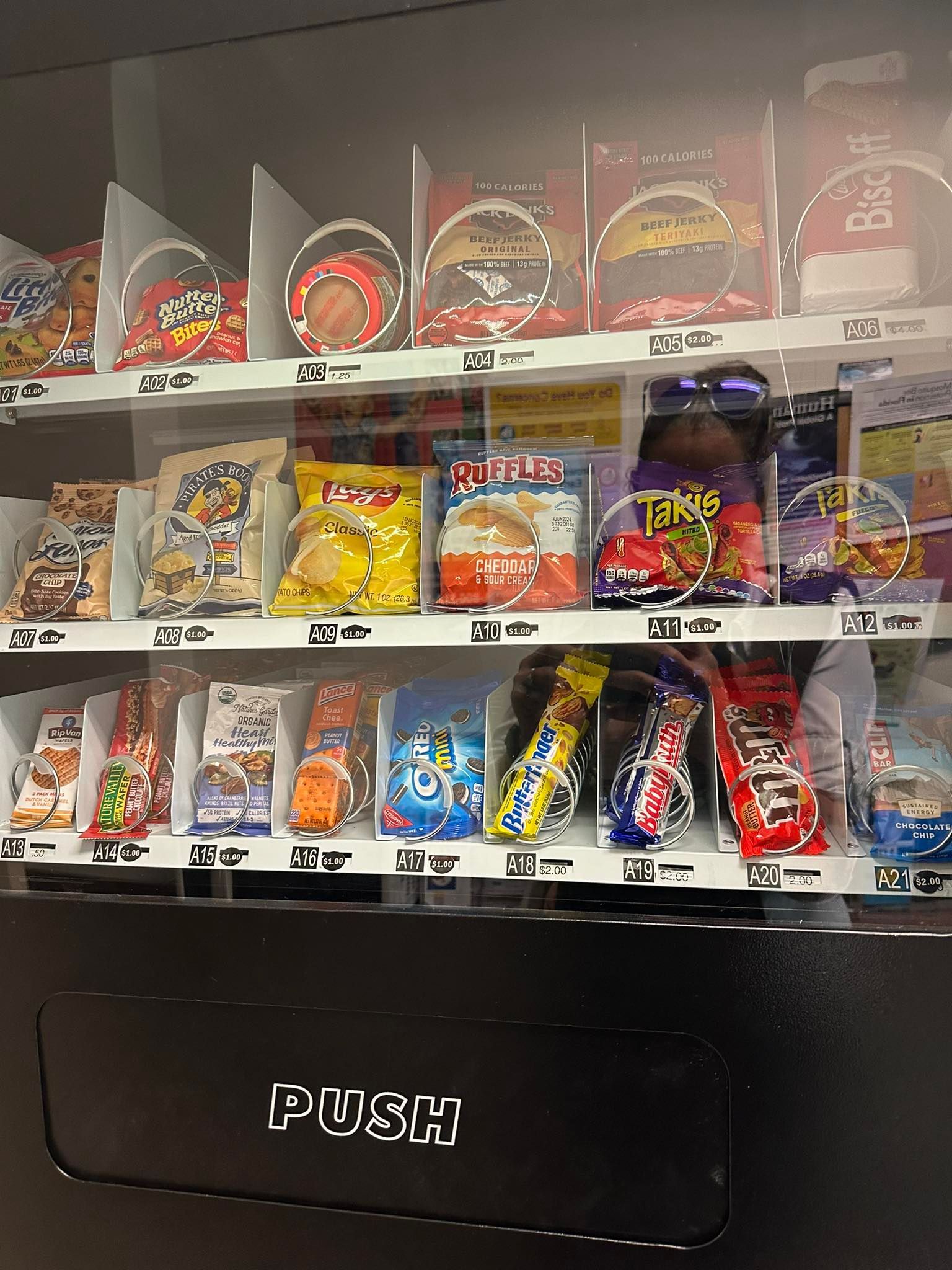 A glass-fronted vending machine filled with various chips, snacks, and candy bars, with a black 'PUSH' door at the bottom.