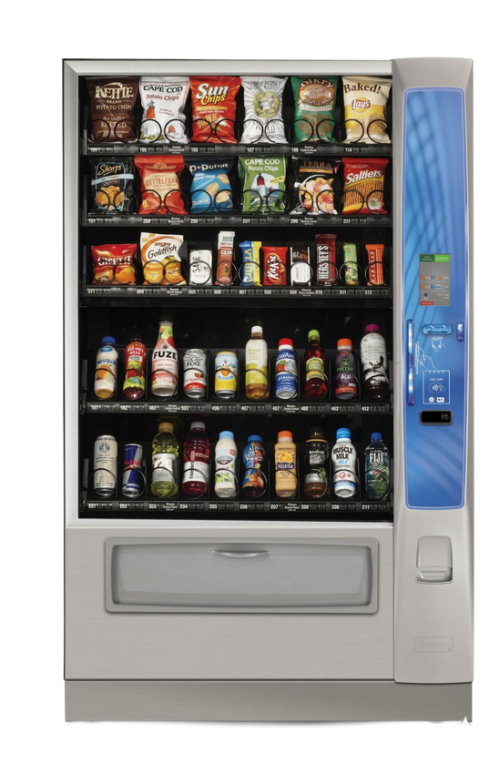 A silver snack and drink vending machine with glass front shelves containing various packaged foods and beverages.