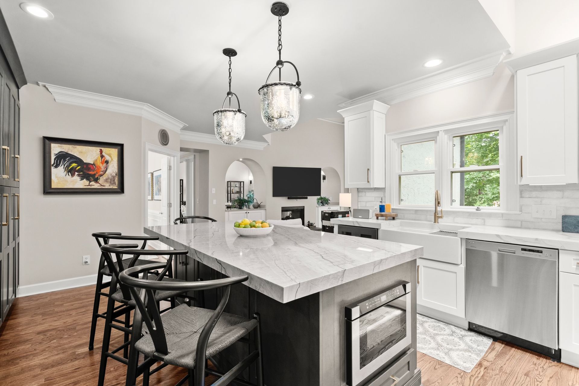 A kitchen with a large island , white cabinets , stainless steel appliances , and hardwood floors.