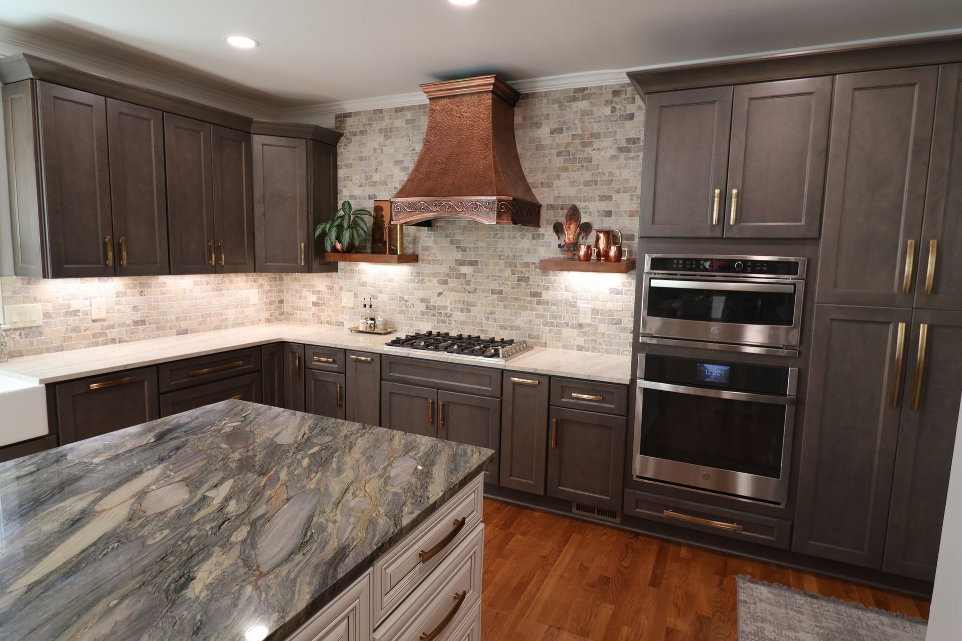A kitchen with gray cabinets , granite counter tops , stainless steel appliances and a copper hood.