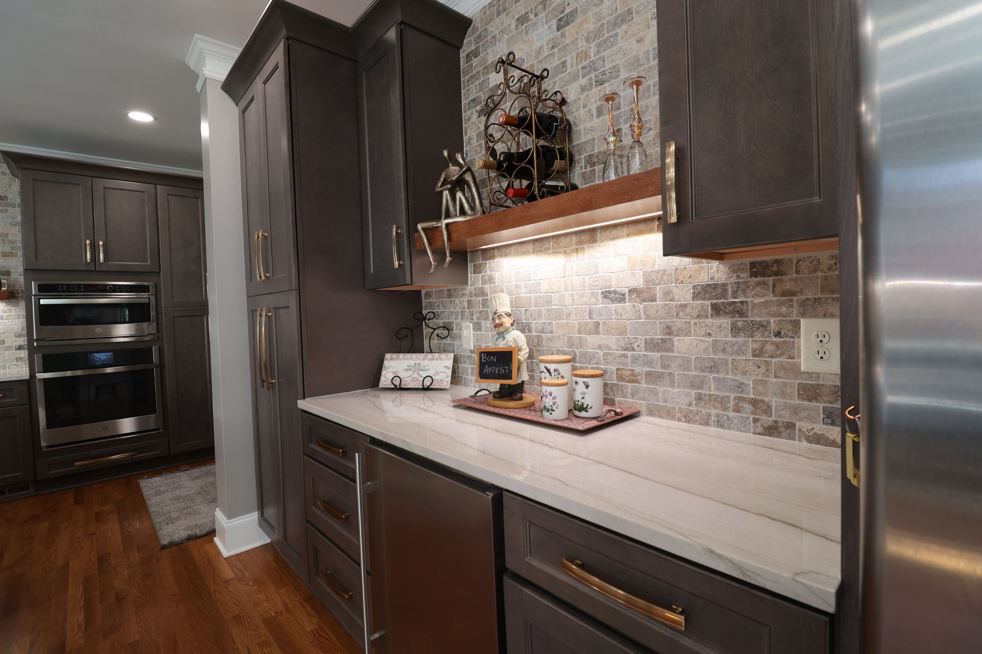 A kitchen with stainless steel appliances , gray cabinets , and a brick wall.