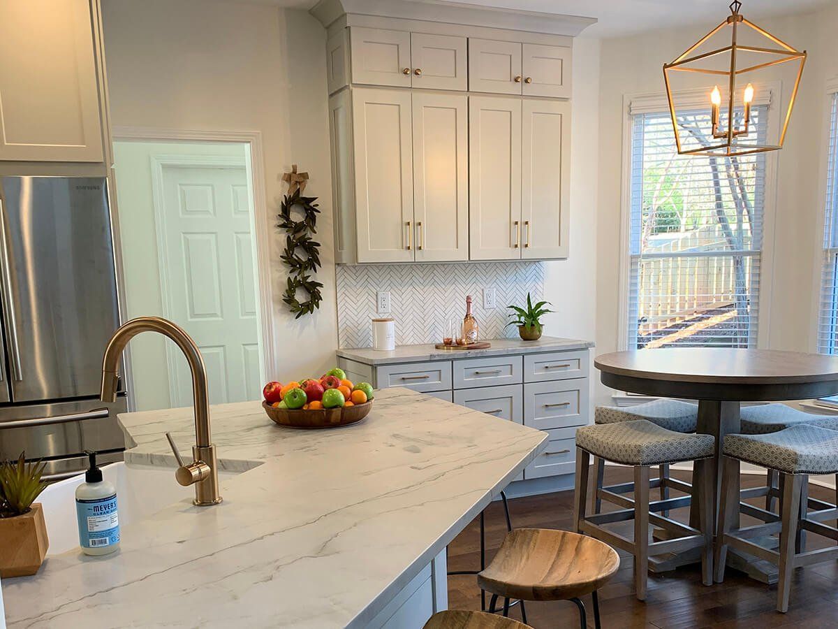 A kitchen with white cabinets , a sink , a table and stools.