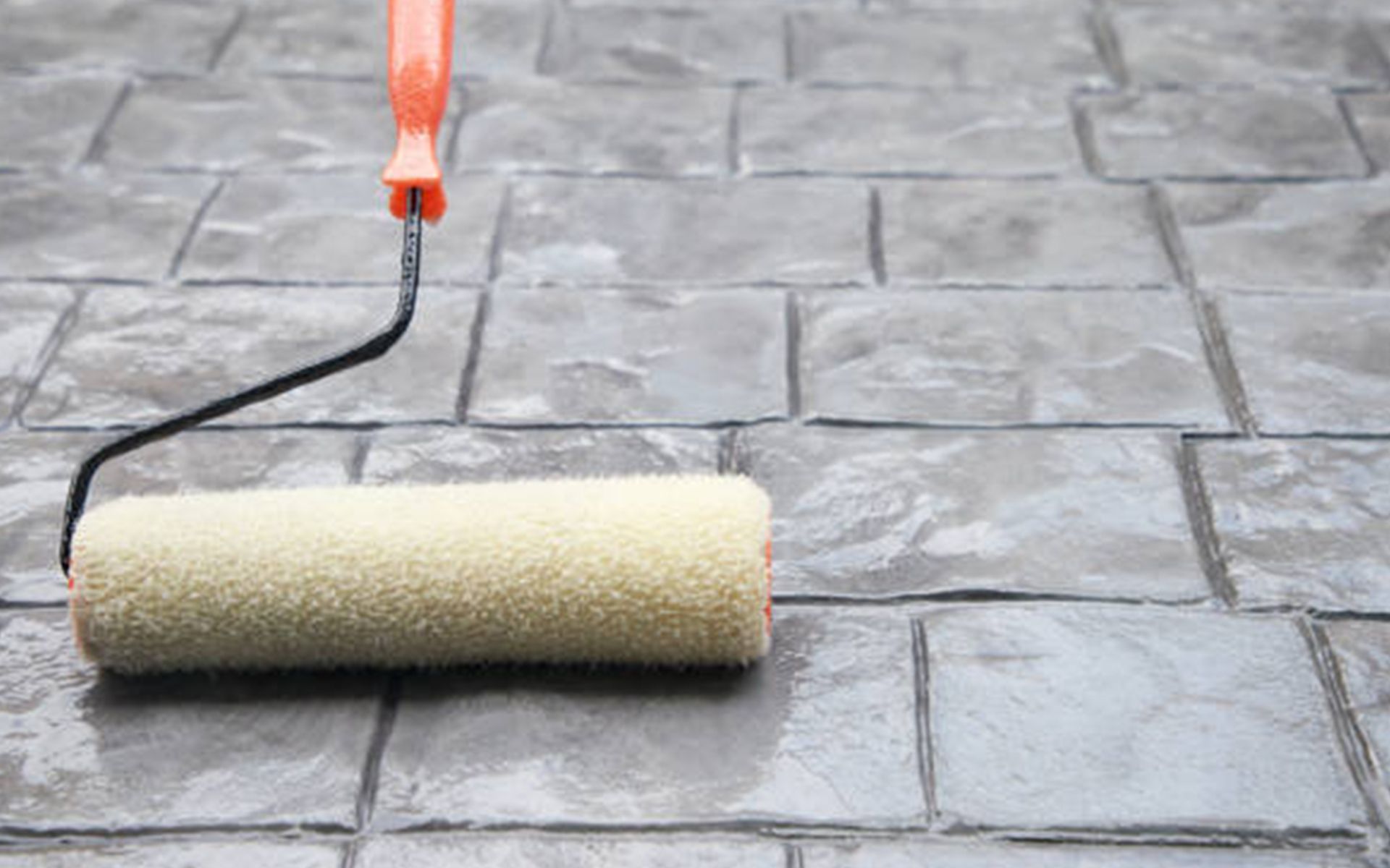 A paint roller is sitting on a brick floor.