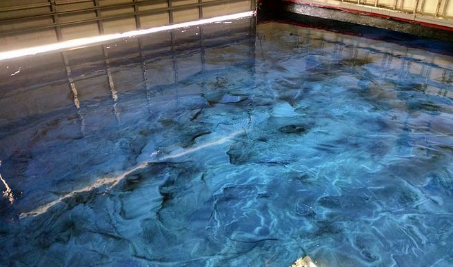 A swimming pool filled with blue water and a reflection of a building in the water.