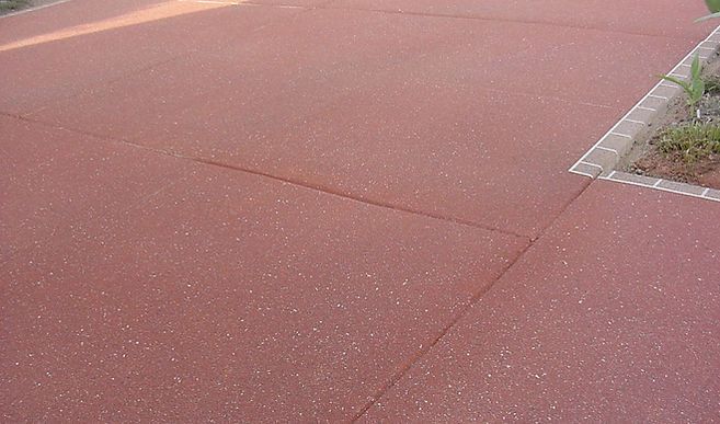 A close up of a red concrete driveway with a tree in the background.