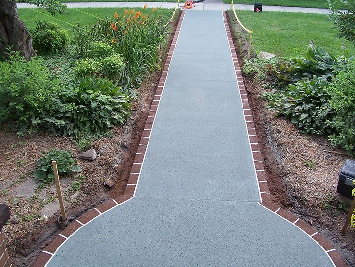 A concrete walkway with a brick border going through a garden