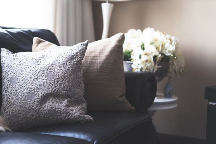 Throw pillows on a black couch next to a side table with white roses