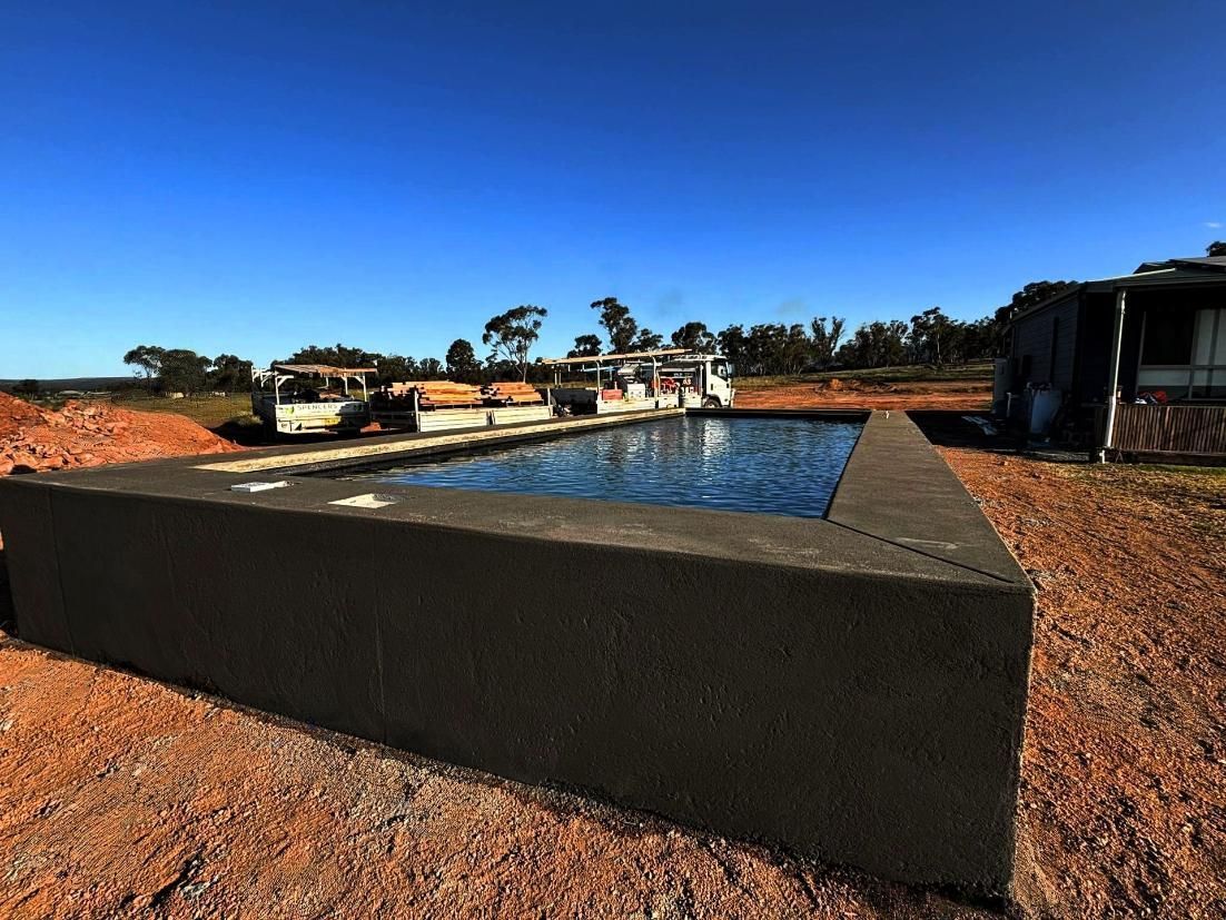 A Large Swimming Pool is in the Middle of a Dirt Field — Spencer's Landscape Construction & Concreting Pty Ltd in Forbes, NSW