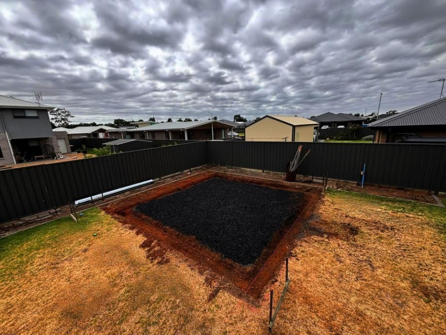 A Large Hole in The Ground in A Backyard with A Fence — Spencer's Landscape Construction & Concreting Pty Ltd in Dubbo, NSW