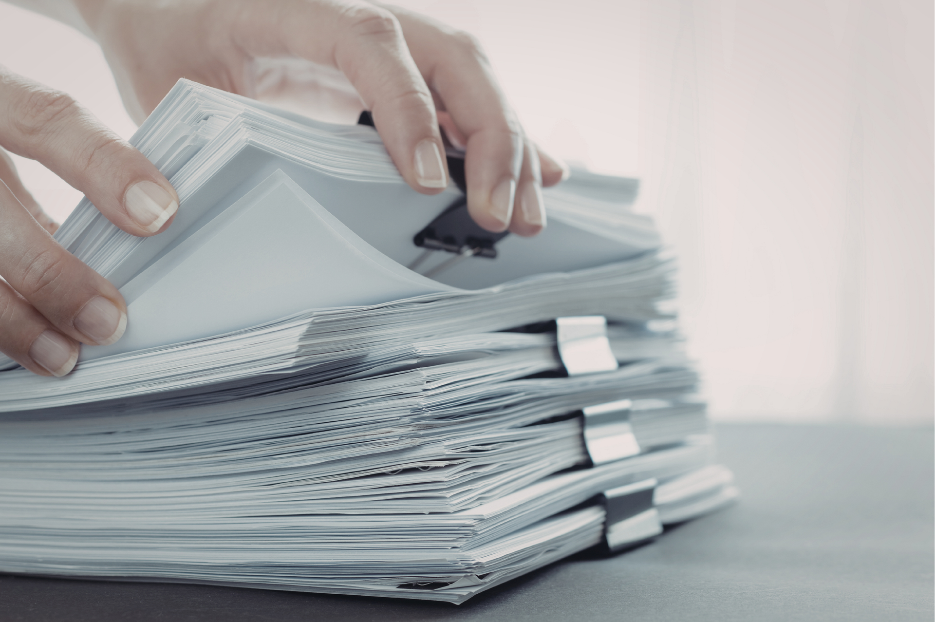 Hands flipping through a thick stack of white papers, secured with binder clips.