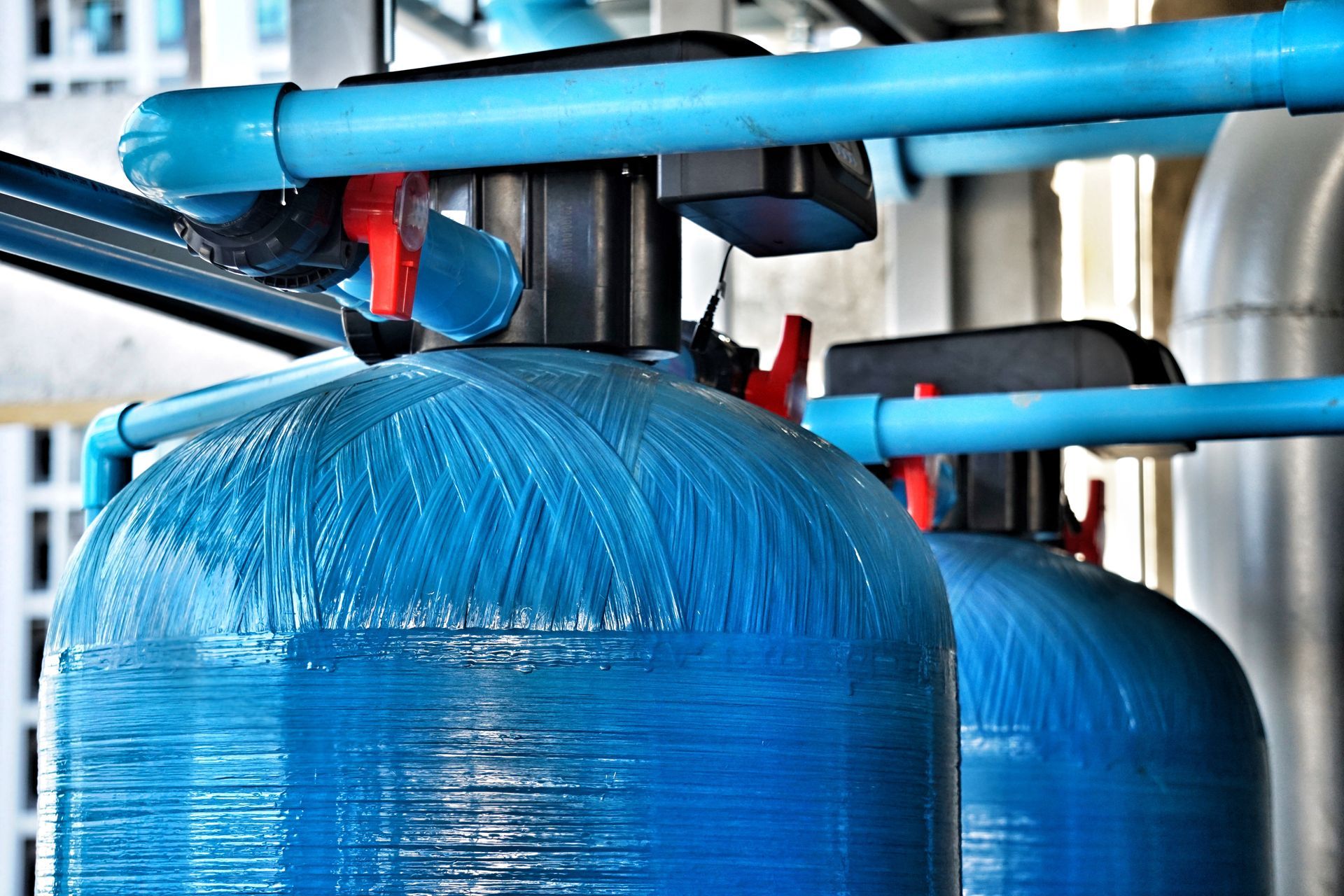 Two blue water tanks are sitting next to each other in a factory.