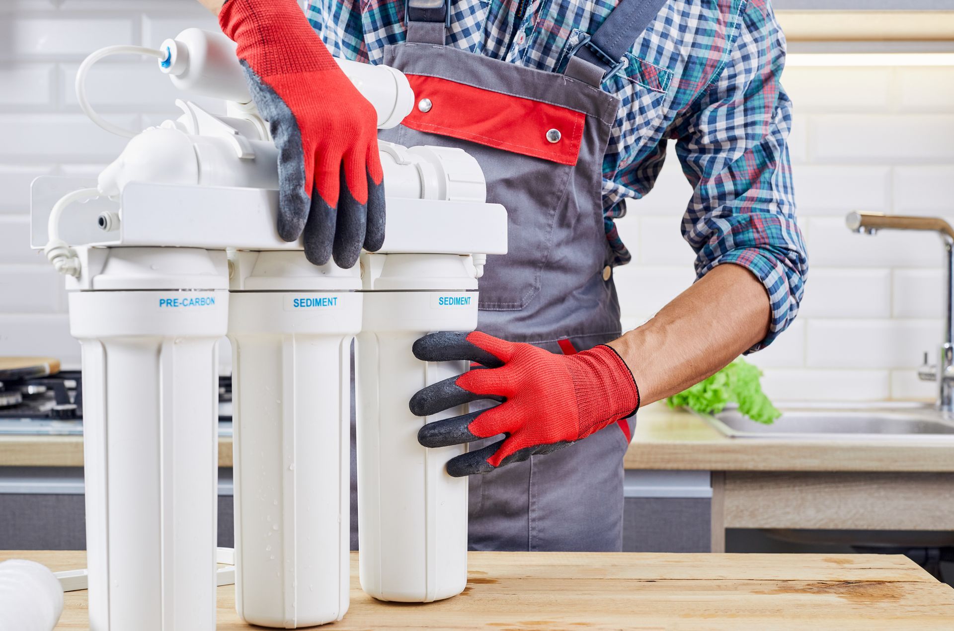 A man wearing red gloves is working on a water filter in a kitchen.