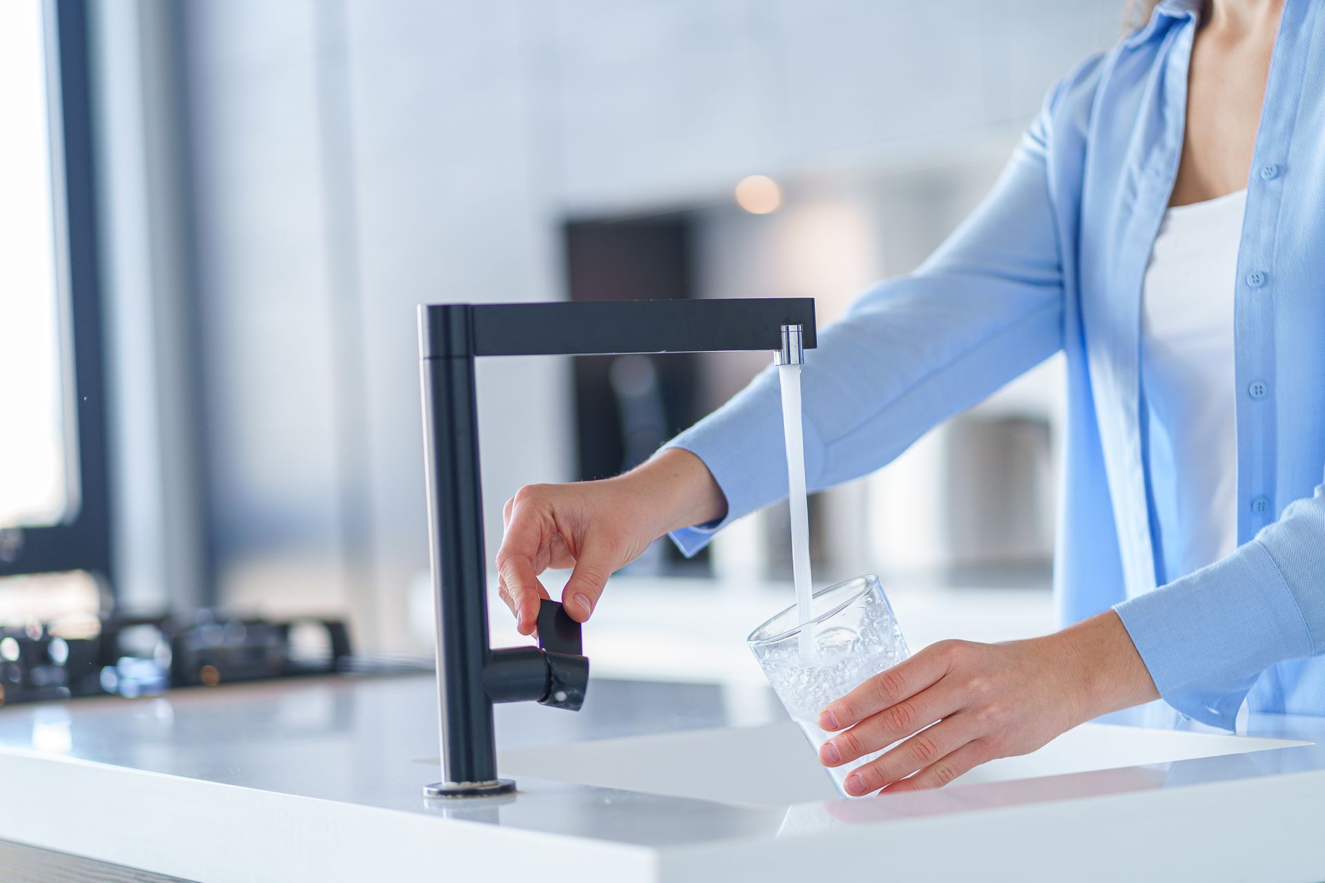 A woman is pouring water from a faucet into a glass.