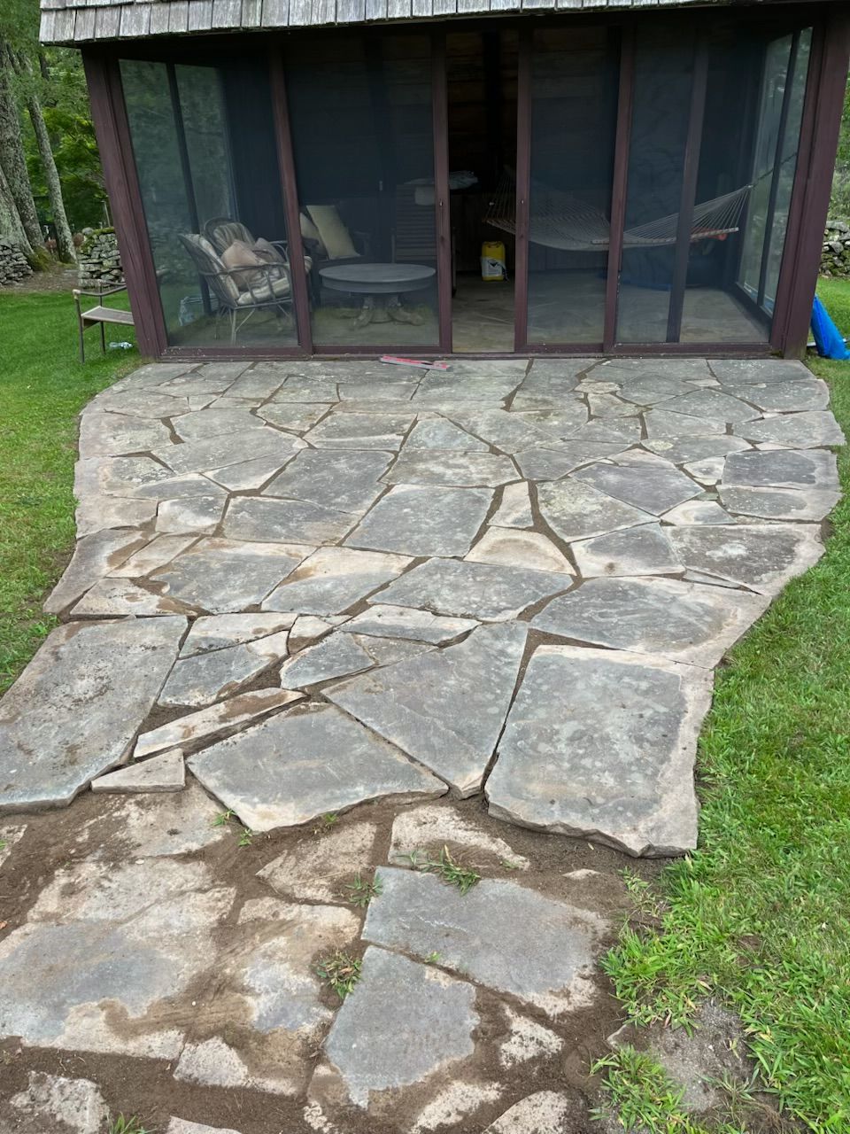 Person wearing red gloves placing a gray brick paver on a bed of gravel.