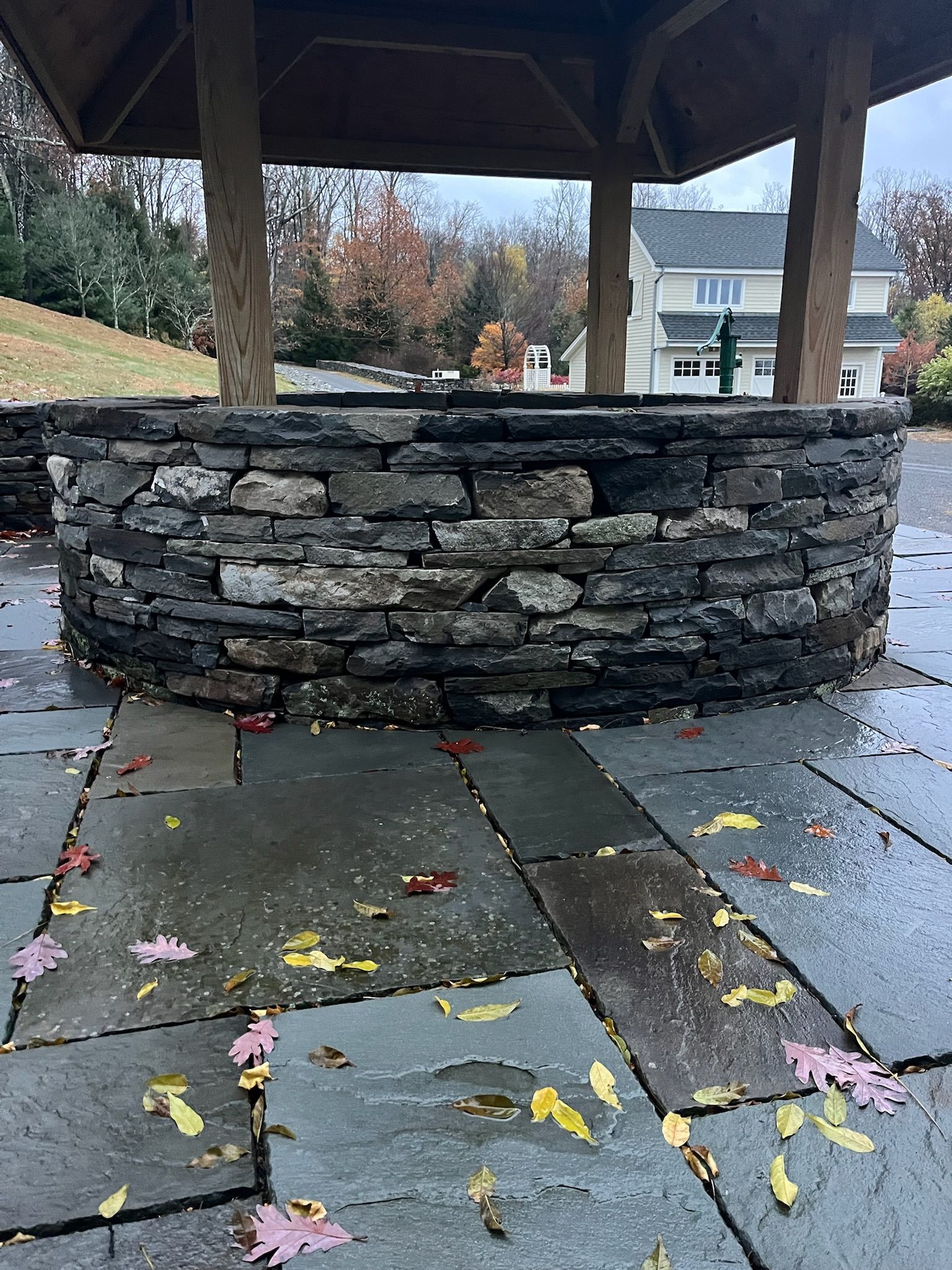 Outdoor living area with wooden furniture, TV, and bar in a shaded structure.