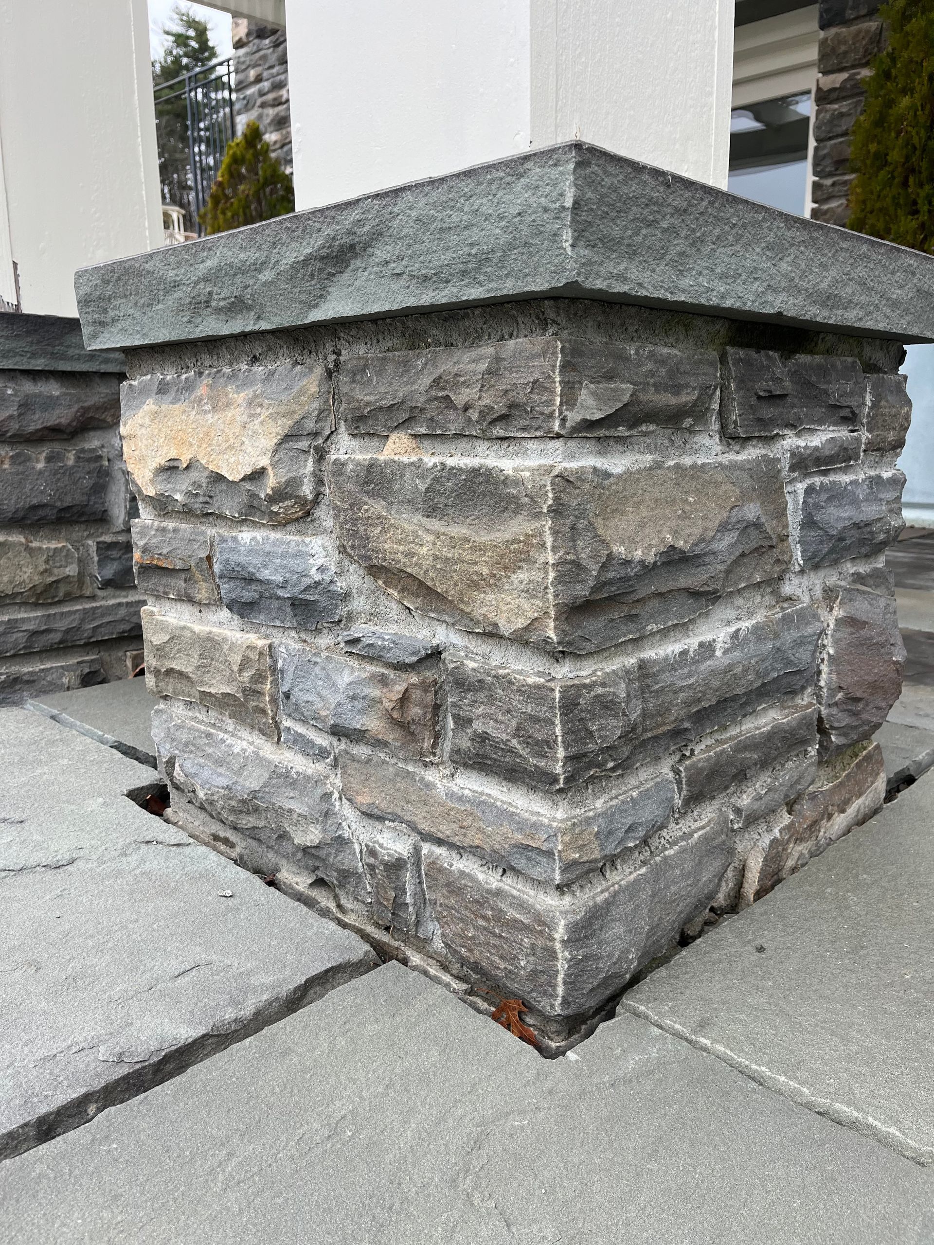 A square stone pillar with a flat cap, situated outdoors on a paved patio surface.