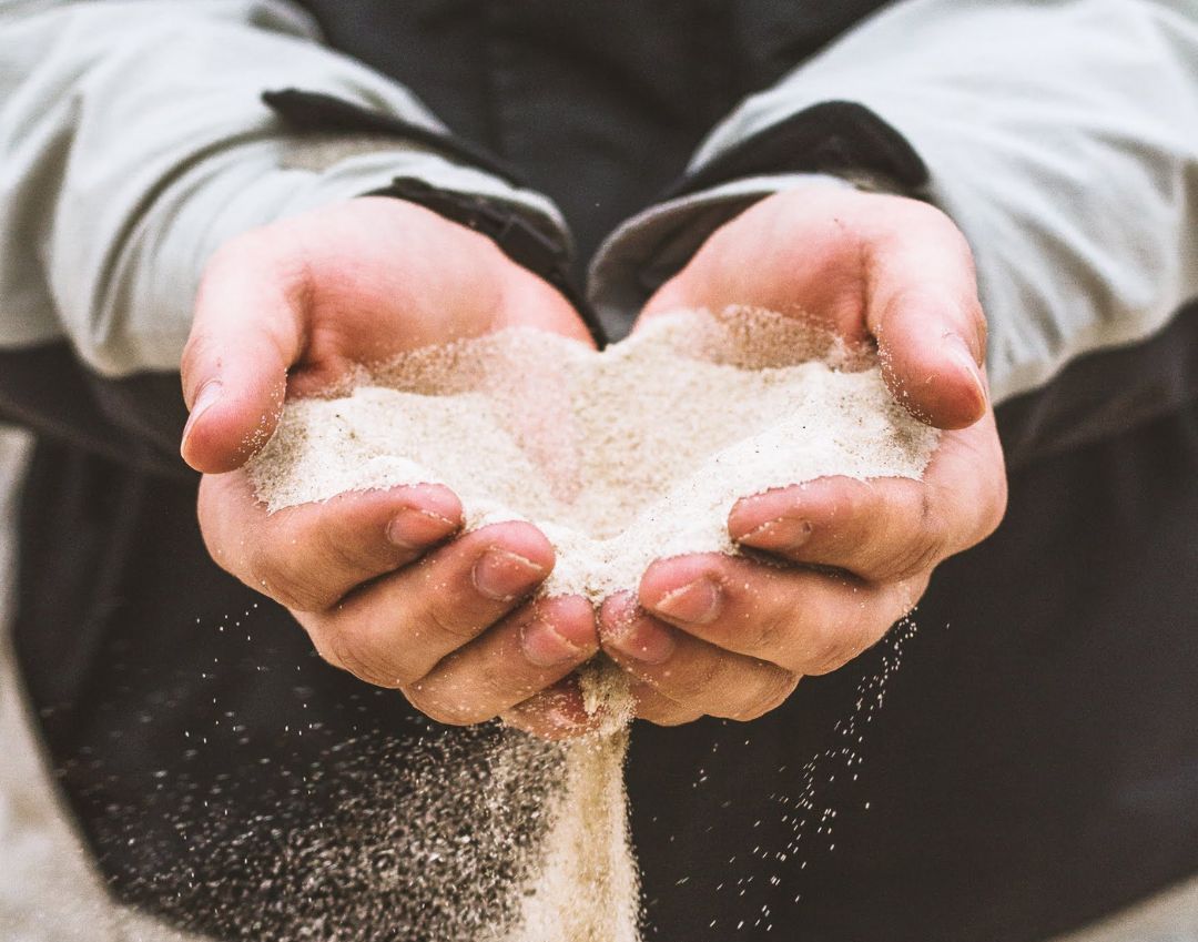 Een persoon houdt zand in zijn handen in de vorm van een hart.