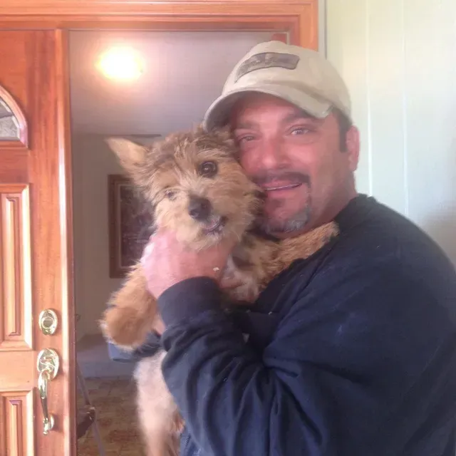 A man is holding a small dog in his arms in front of a door in South Bay, CA