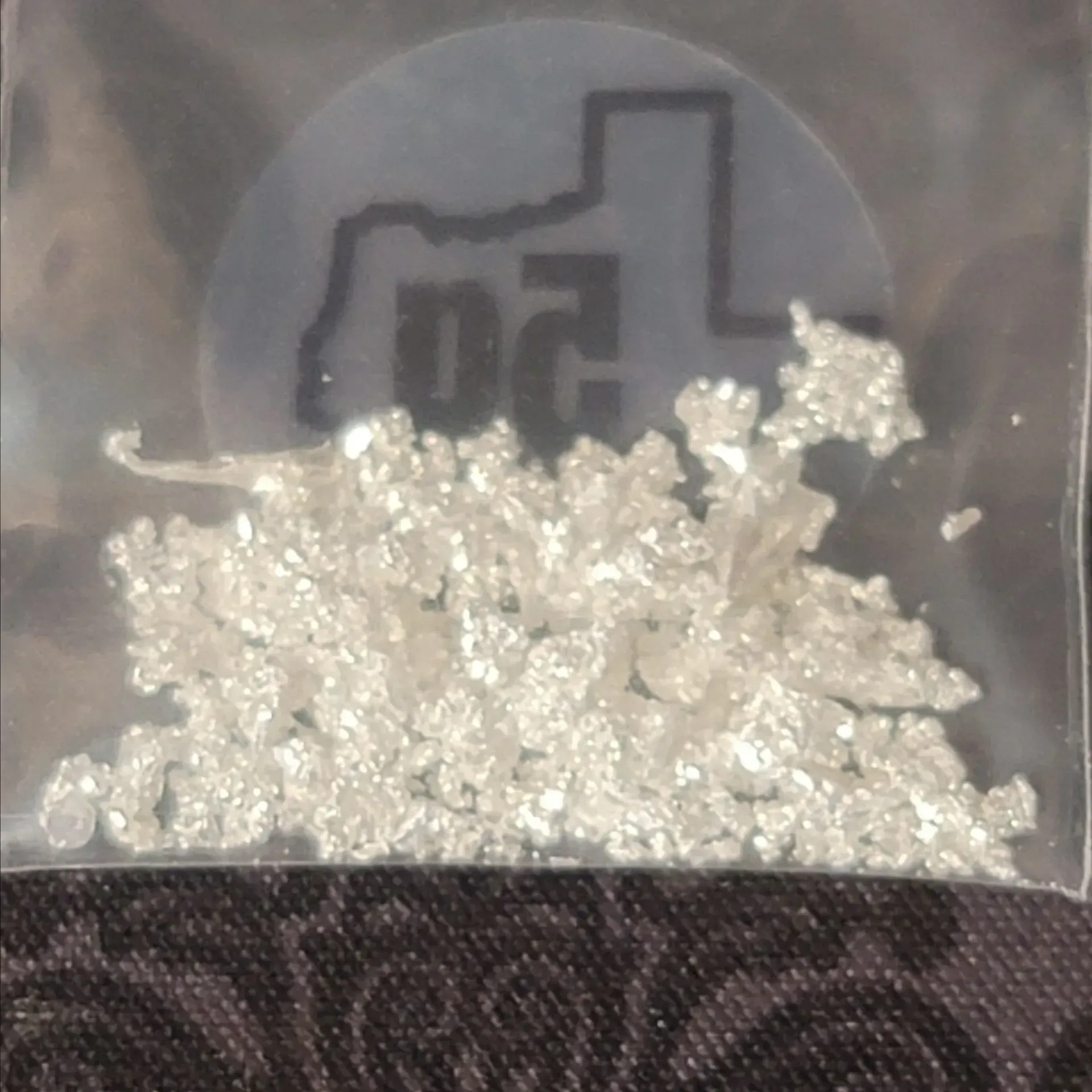 A small plastic bag containing silver crystalline material. It has a Texas-shaped sticker indicating 5g, from ETG&S.