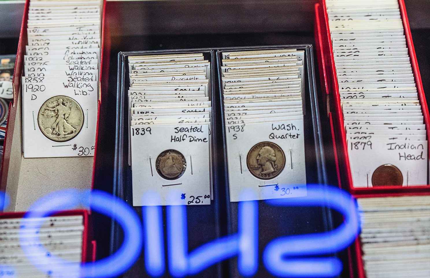 Coin display with labeled coins in red trays, visible through a blue neon sign.