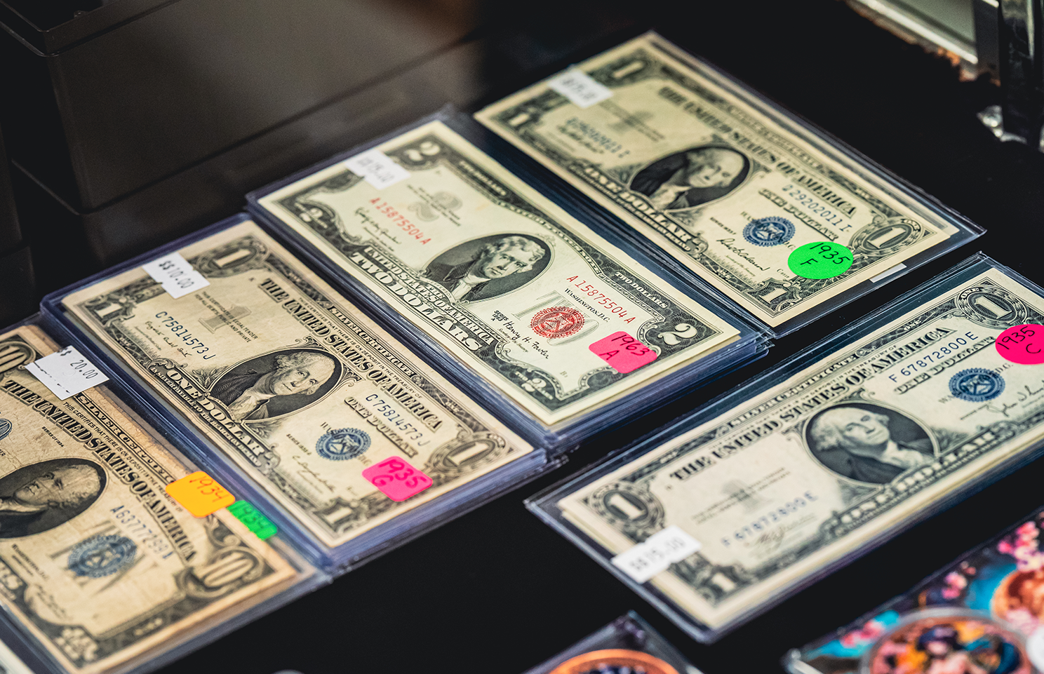 Stacks of old one-dollar bills in protective sleeves, displayed at a sale, with colorful price tags.