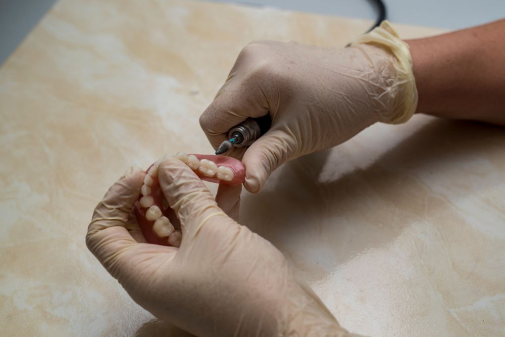 A Person Wearing Gloves Is Grinding A Tooth With A Machine — Dentures in Port Macquarie, NSW