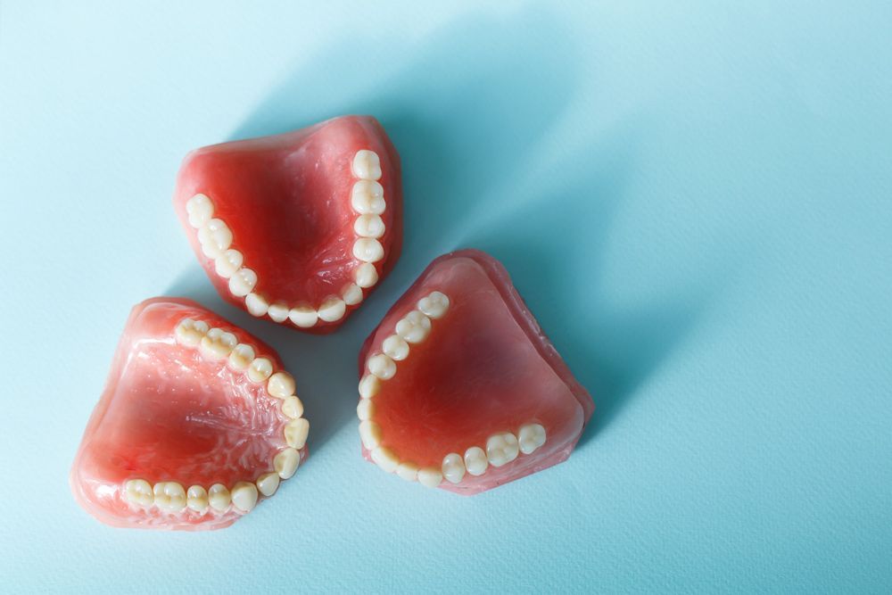 Three Dentures Are Sitting On Top Of Each Other On A Blue Surface — Dentures on the Central Coast, NSW