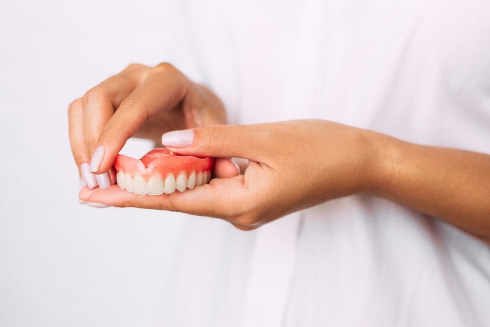 A Woman Is Holding A Partial Denture In Her Hands — Dentures in Port Macquarie, NSW