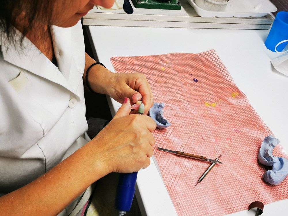 A Woman Is Working On A Denture Besides the Table — Dentures in Glendale, NSW