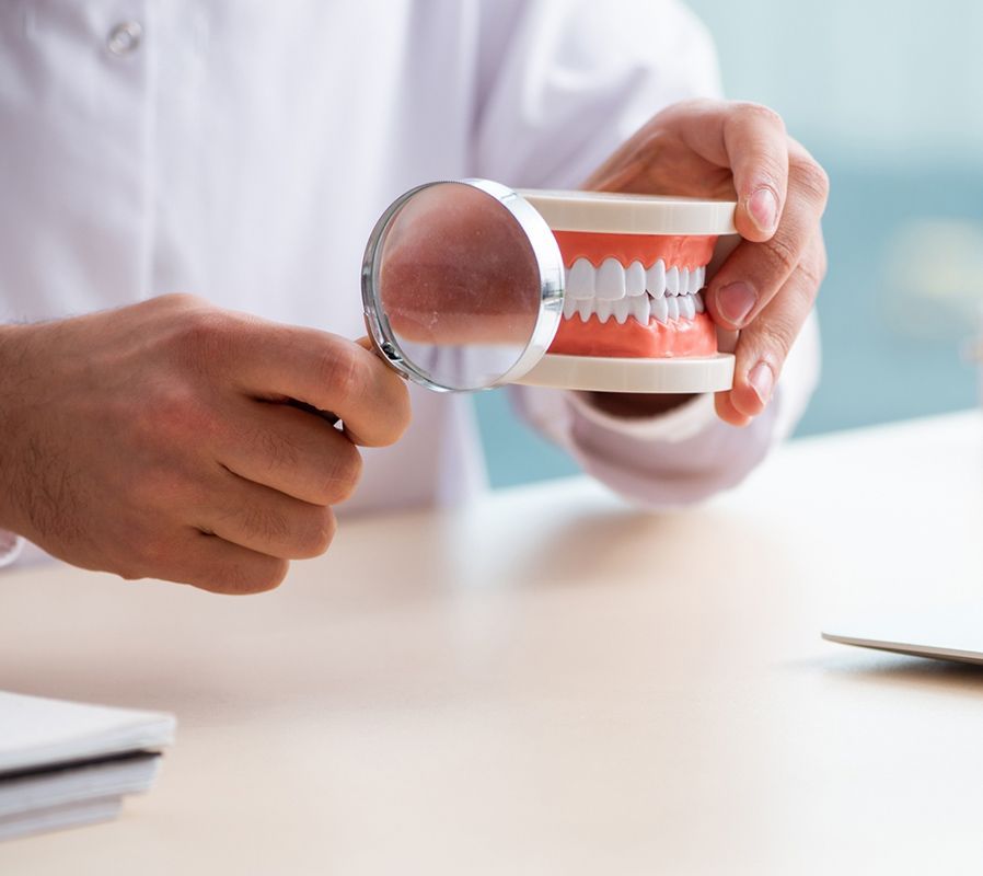 A Dentist Is Examining A Model Of Denture With A Magnifying Glass — Dentures in Long Jetty, NSW