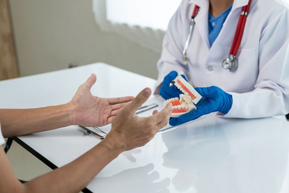 A Dentist Is Holding A Model Of Denture To A Patient — Dentures in Toukley, NSW