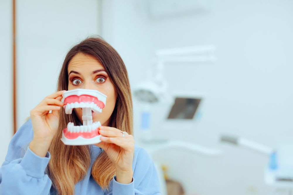 A Woman Is Holding A Model Of Her Denture In Front Of Her Face — Dentures in Gosford, NSW