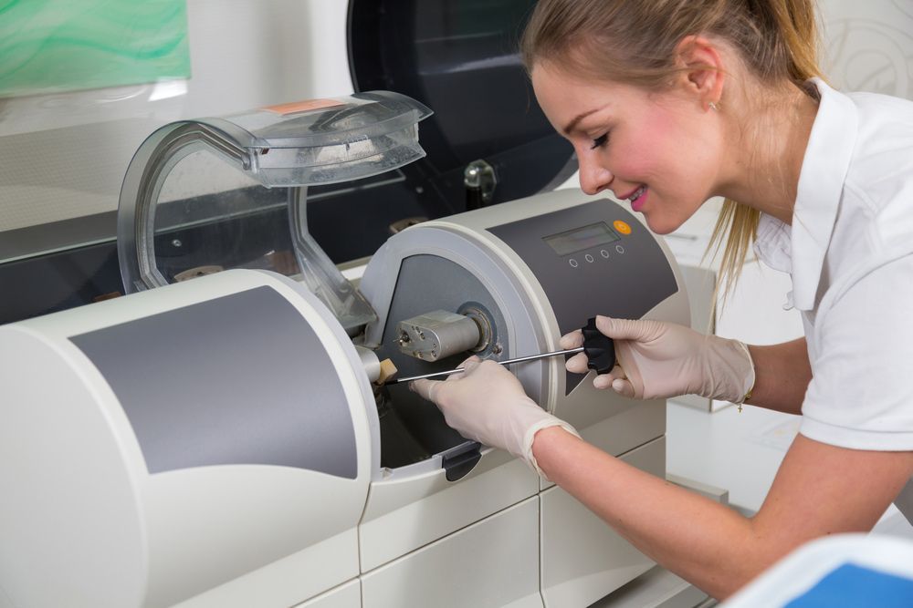 A Woman Is Working On A Machine In A Dental Office — Dentures in Lake Macquarie, NSW
