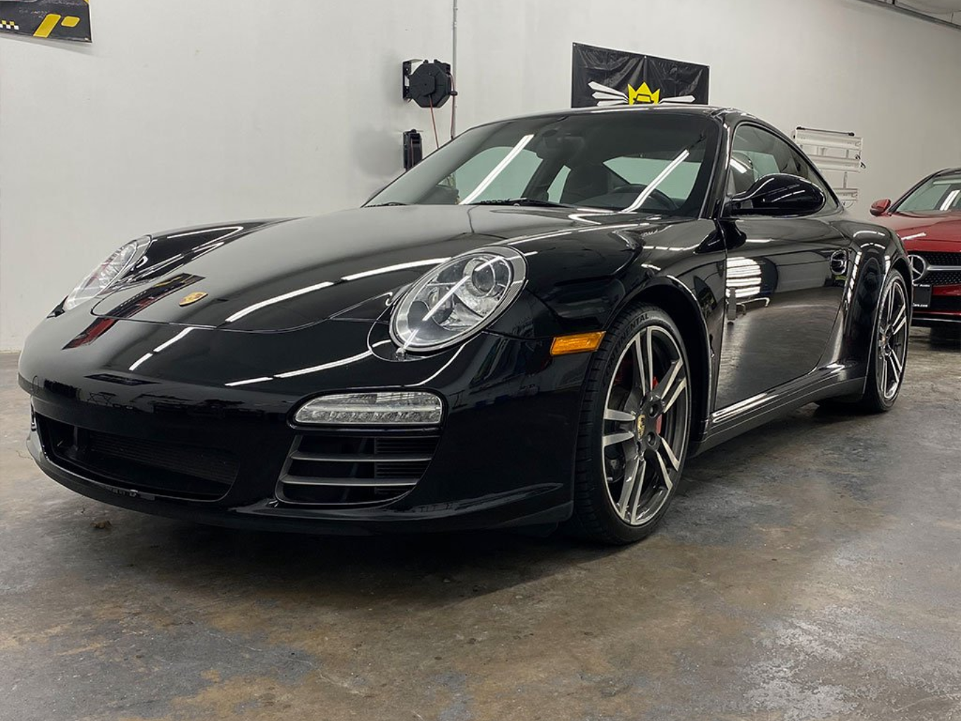 Black Porsche sports car parked inside a garage, glossy finish, gray wheels.