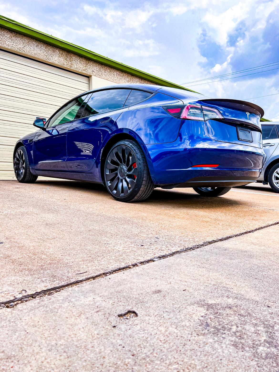 Man holding large clear film in front of a car in a garage.
