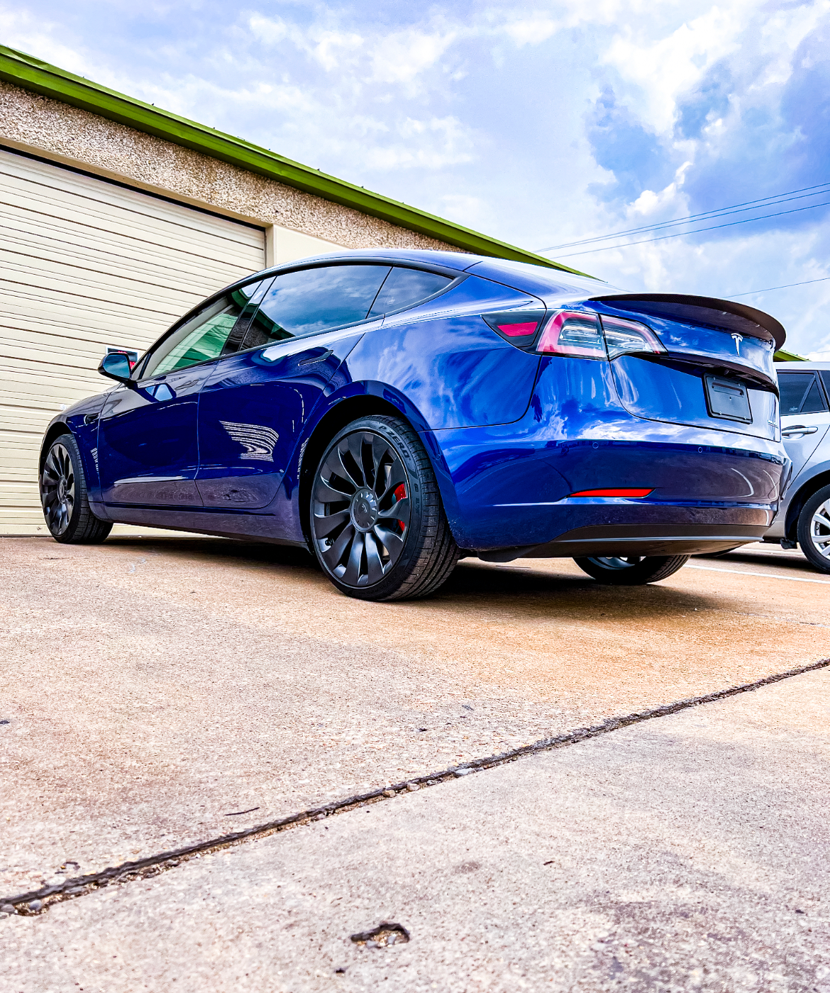 Red Porsche sports car in a shop. Black wheels, tinted windows. Person in background working.