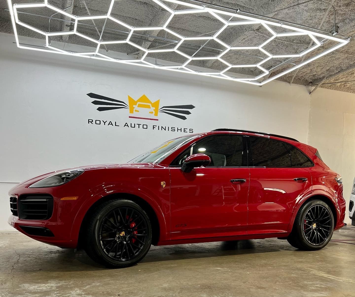A person in a red shirt sprays water on a maroon car at a car wash.