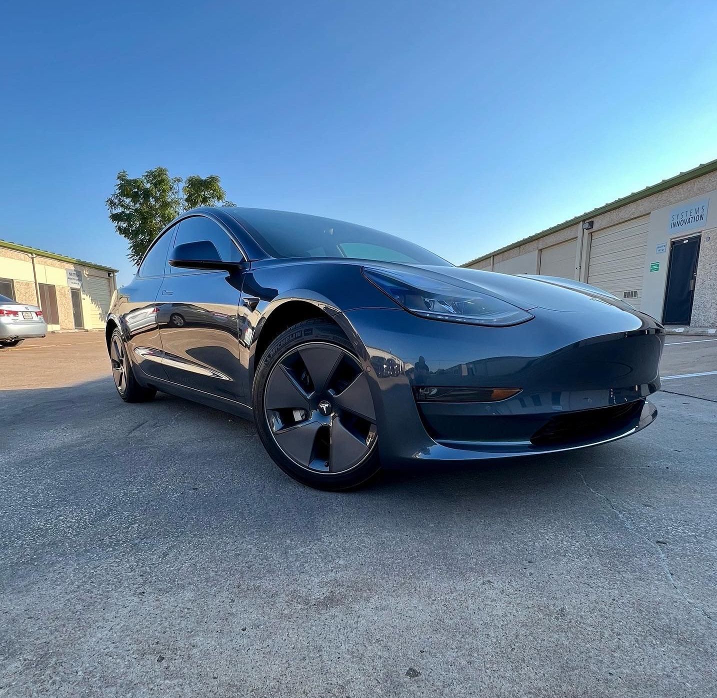 A black tesla model 3 is parked in a parking lot.