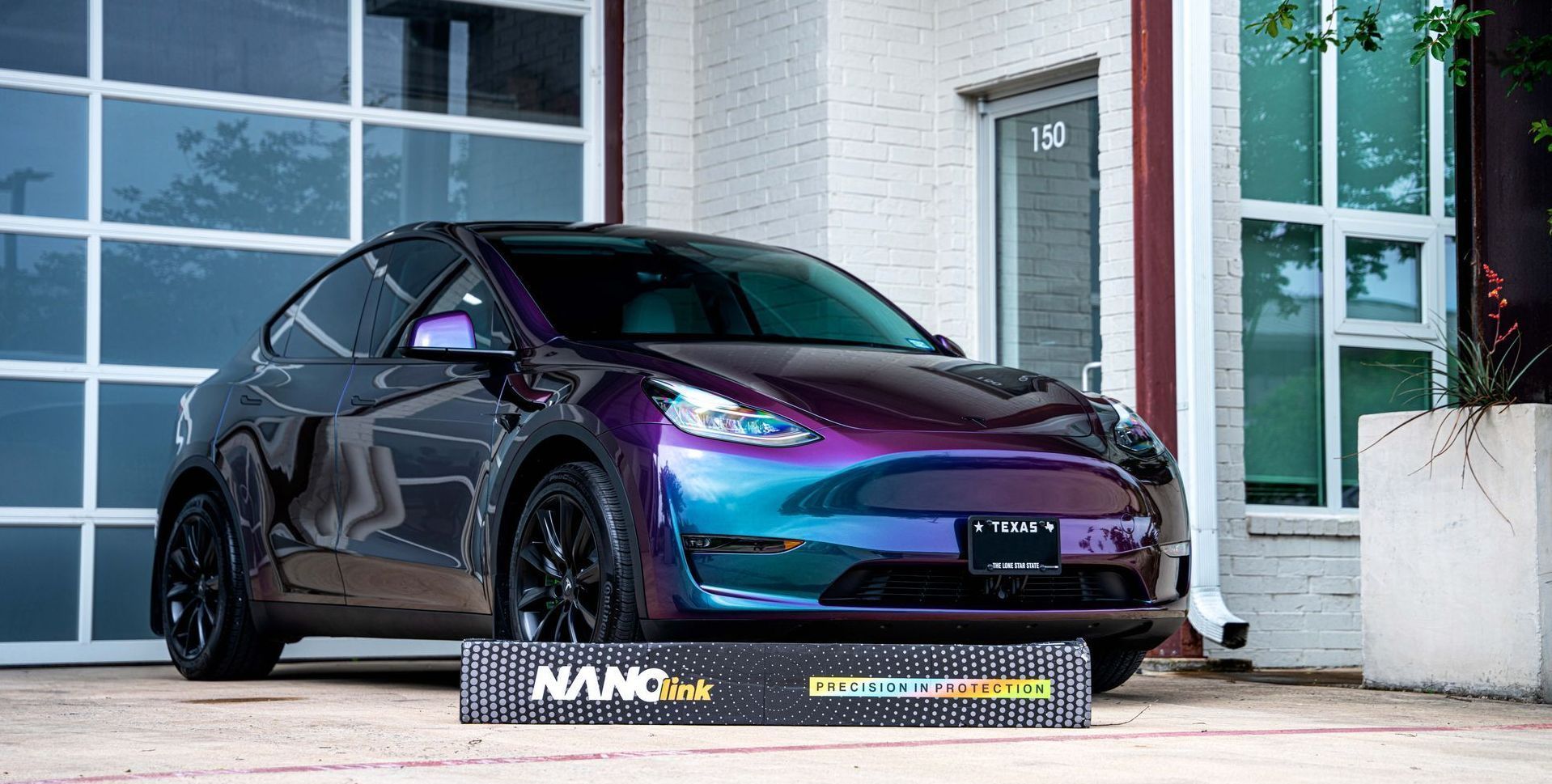 A purple and blue tesla model y is parked in front of a garage door.