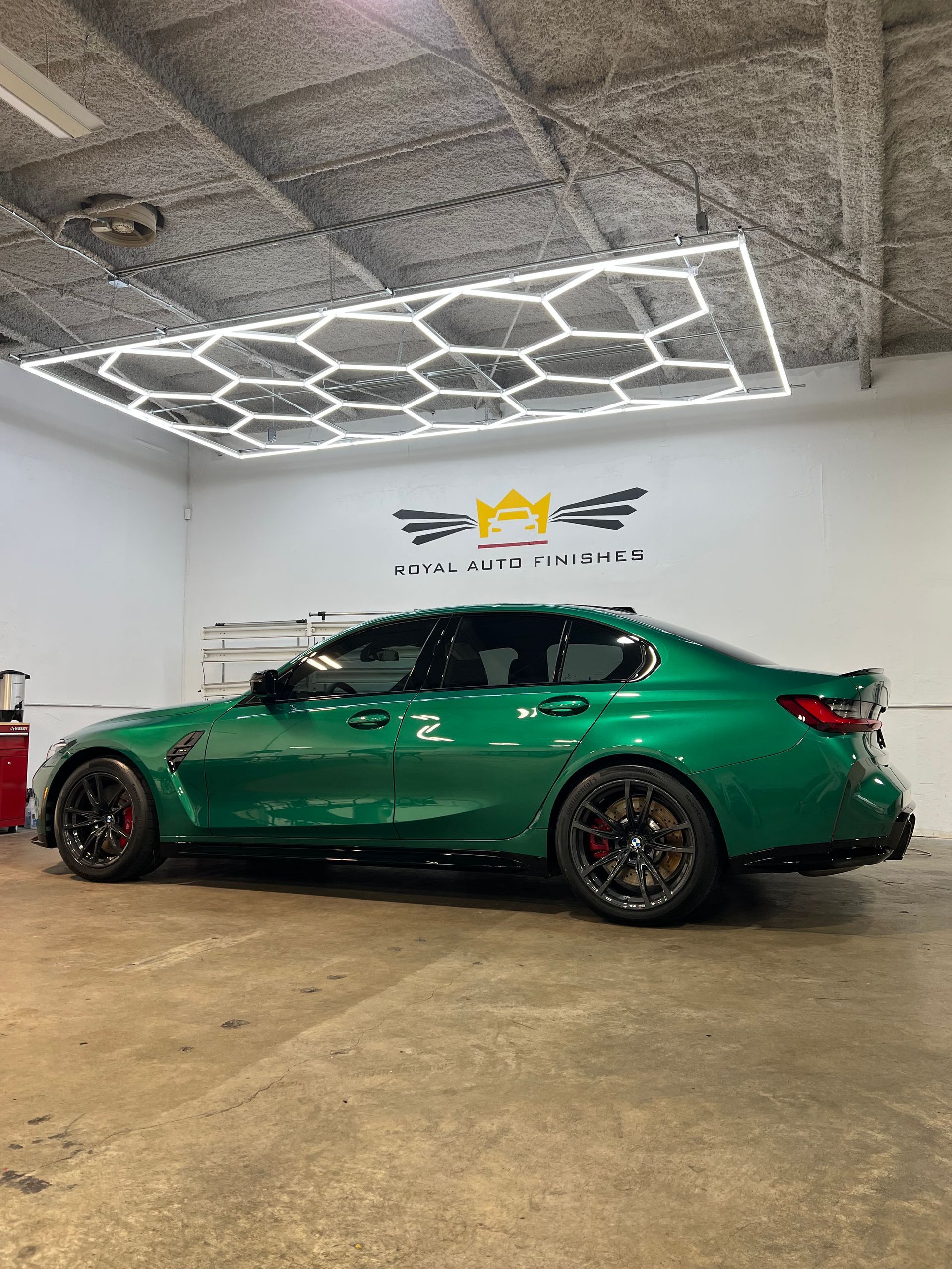 Green BMW sedan parked inside a garage with hexagon-shaped lighting.