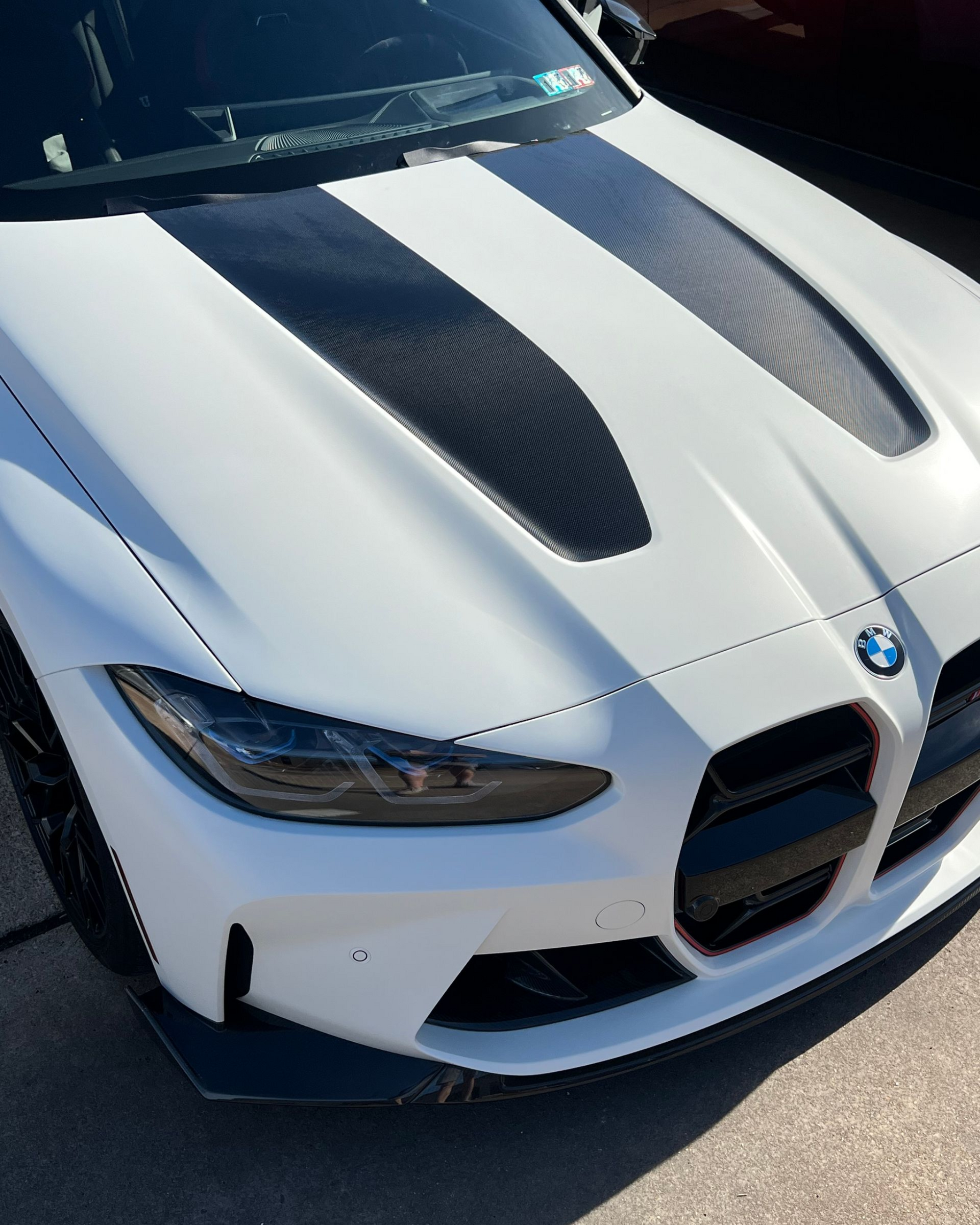 White BMW sports car with black hood stripes and carbon fiber vents.