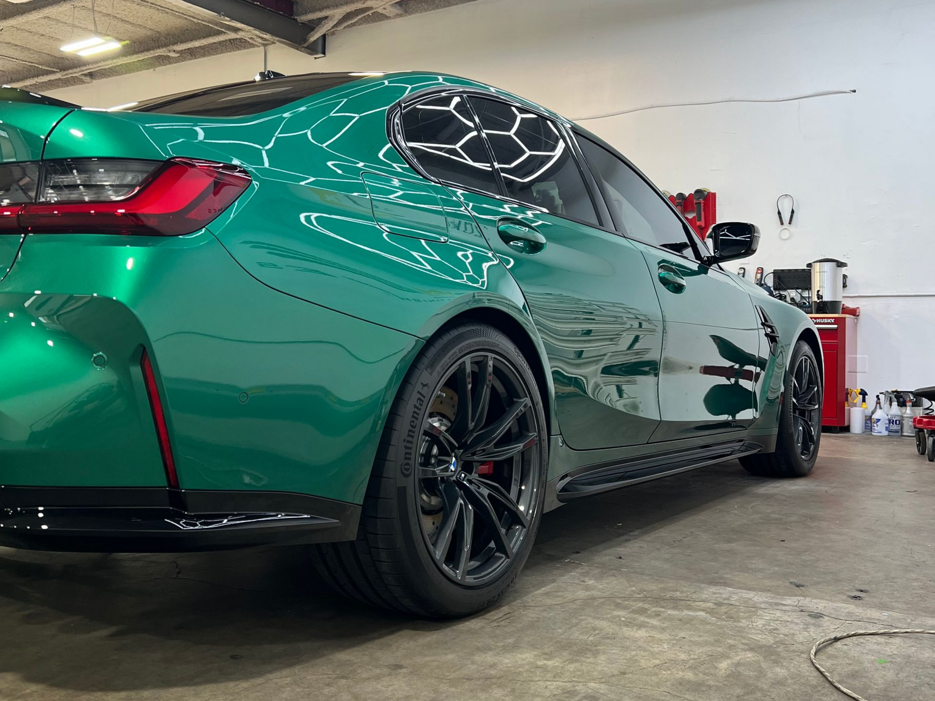 Bright red Porsche 911 coupe in a workshop with black wheels, under bright lights.