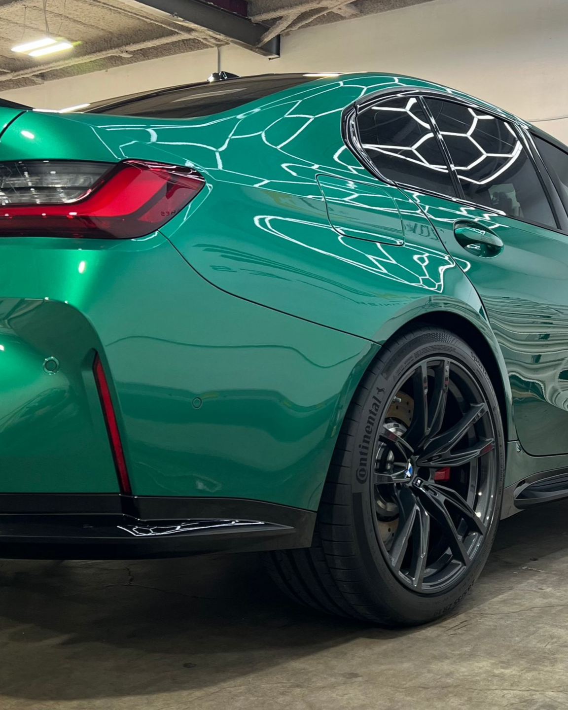 Green BMW M4 parked in front of a building with closed garage doors, against a cloudy sky.
