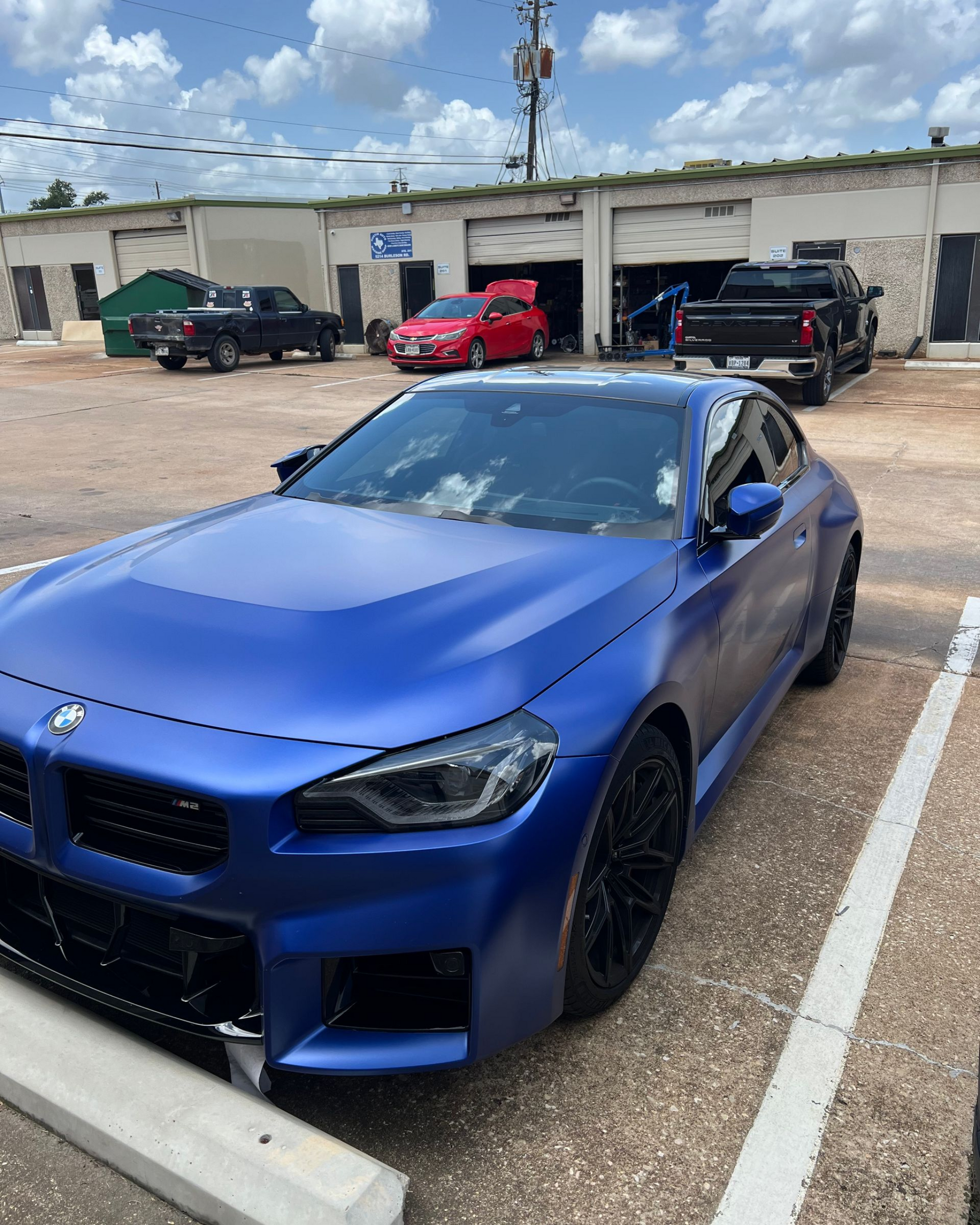 Blue BMW sports car parked outside a building, other vehicles in the background.