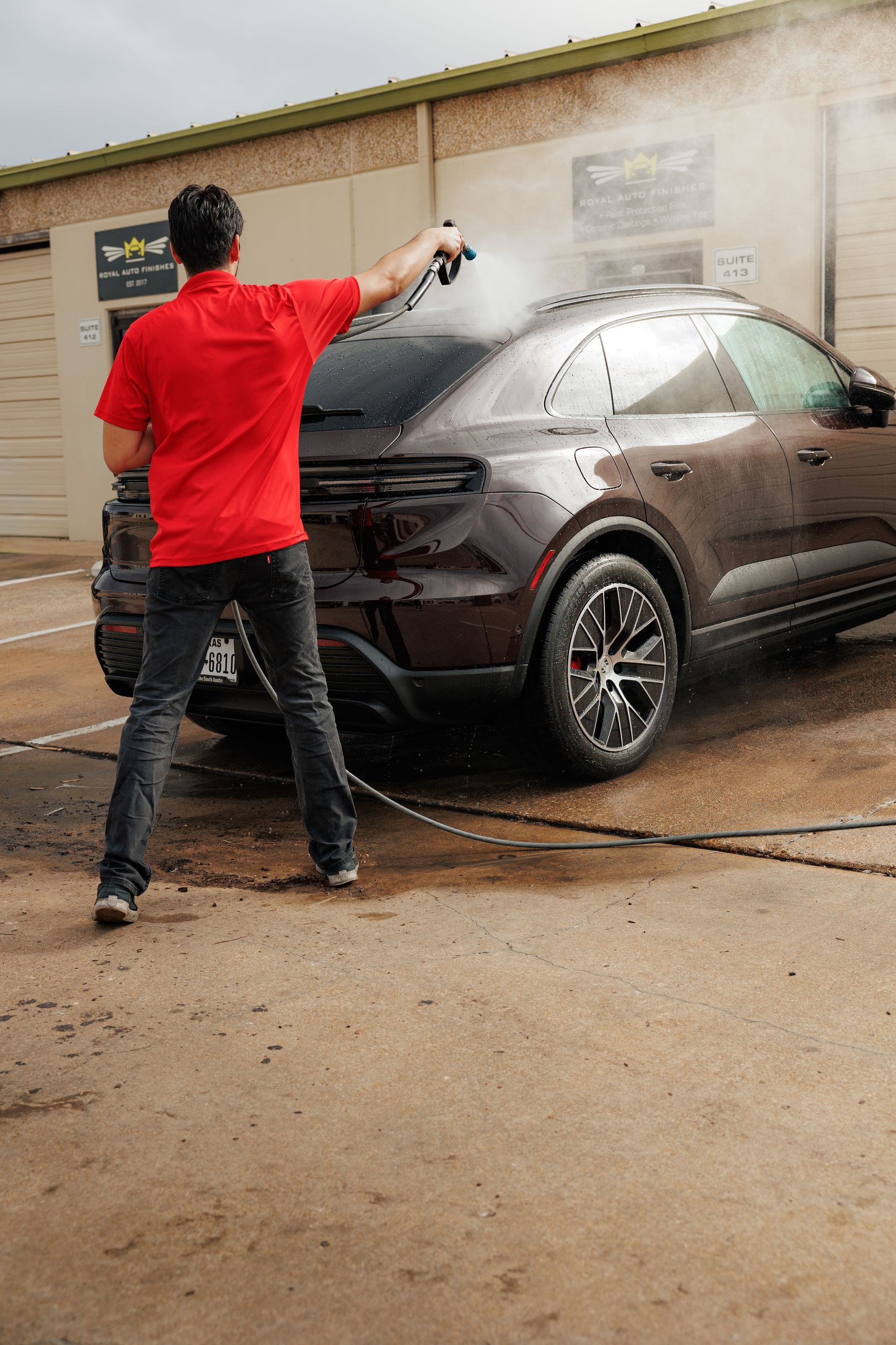 Man holding large sheet of clear film with water droplets, near a white car in a garage.