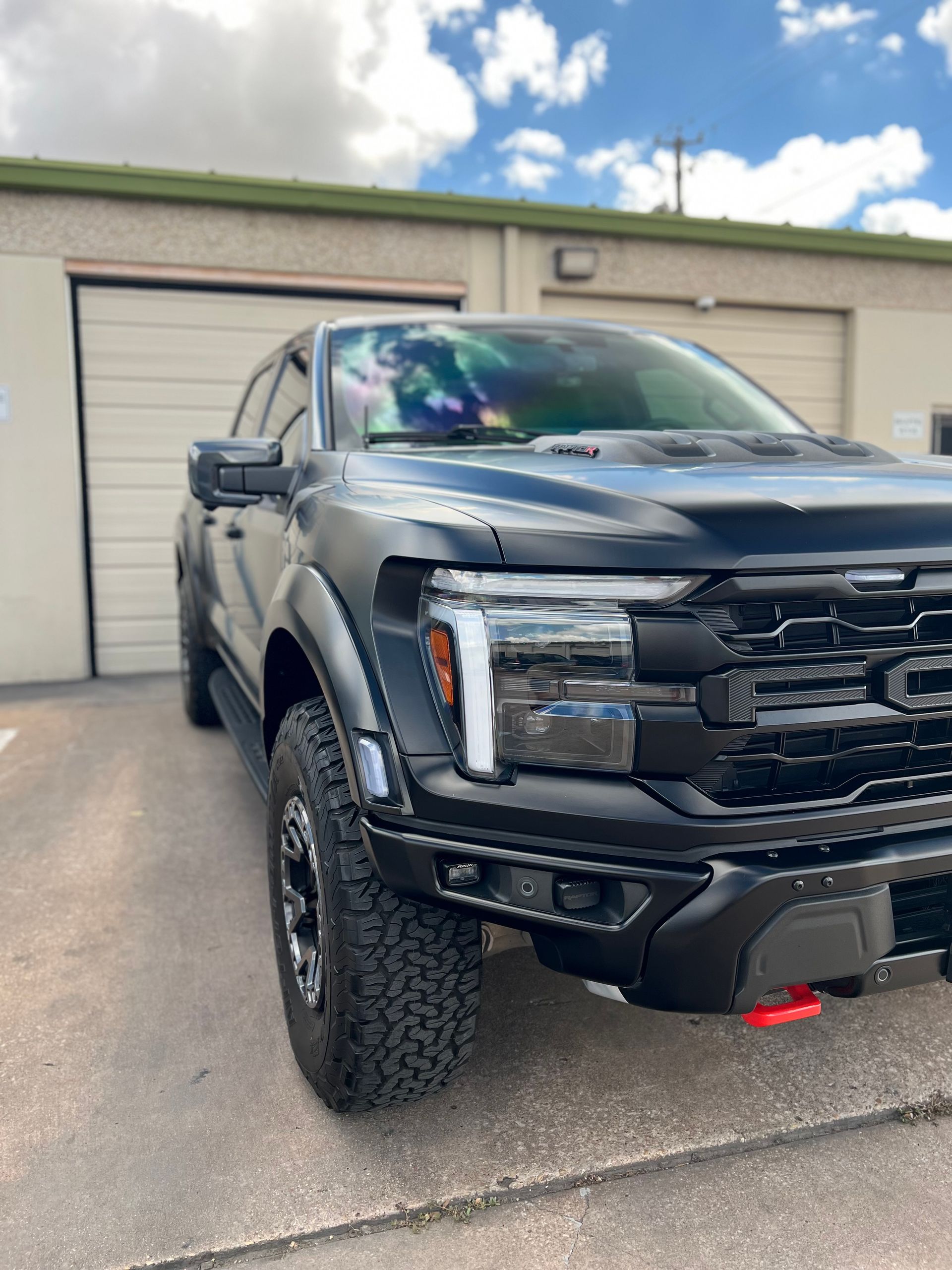 Man holding clear plastic sheet with water droplets, near a silver car in a garage.