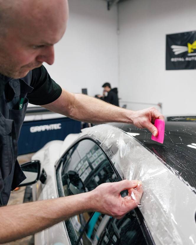 A person applying film to a car window with a pink squeegee in a shop.