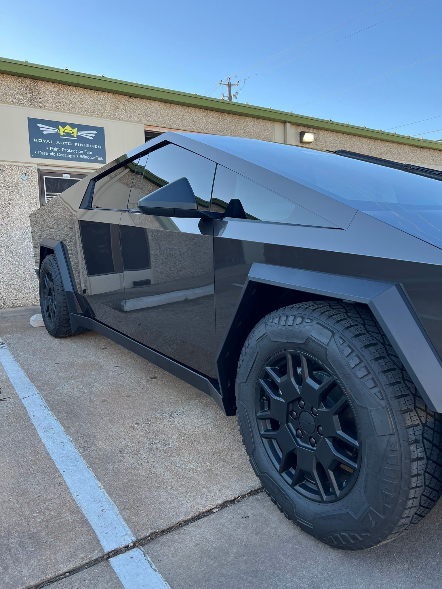 A black car is parked in a parking lot in front of a building.